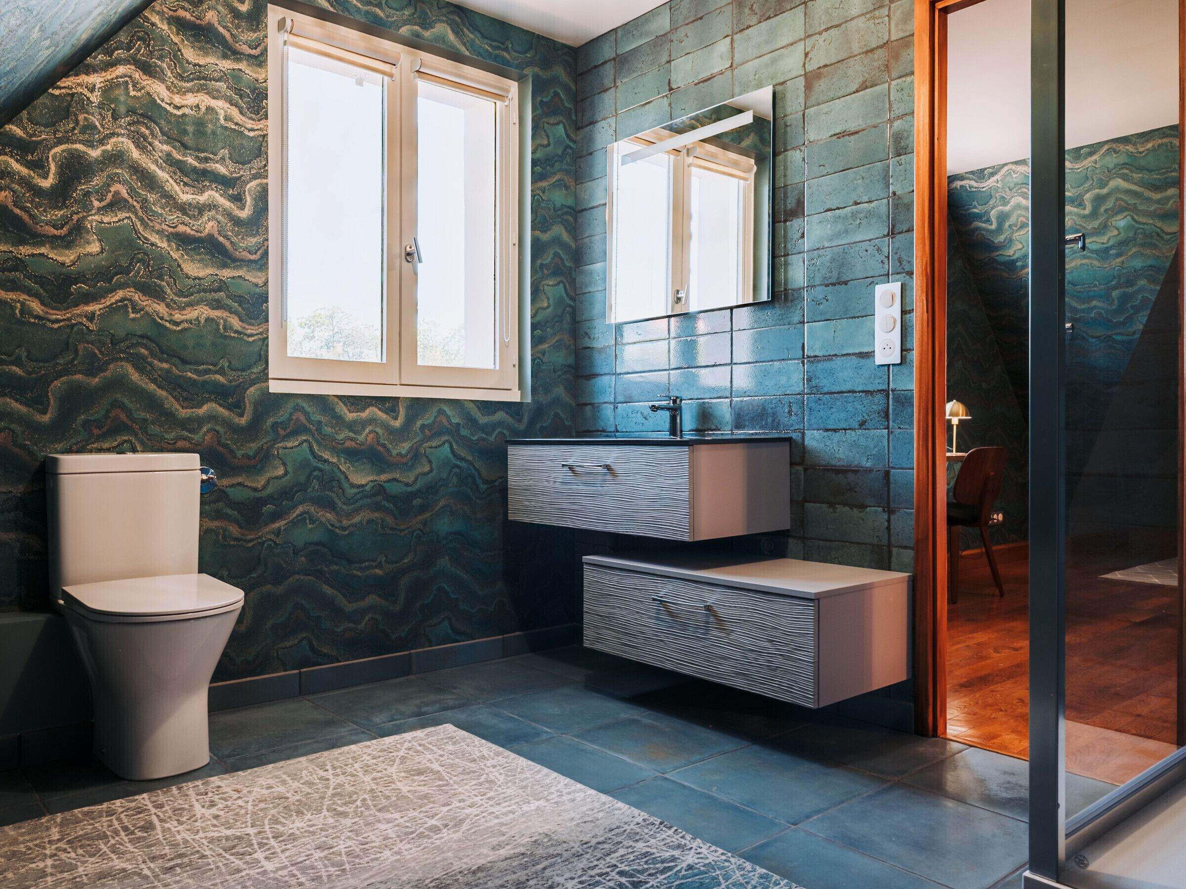 Un baño con pared de mármol, inodoro, lavabo y espejo.