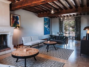 Uma sala de estar moderna com lareira, um sofá, duas mesas redondas e um espaço de jantar com cadeiras.
