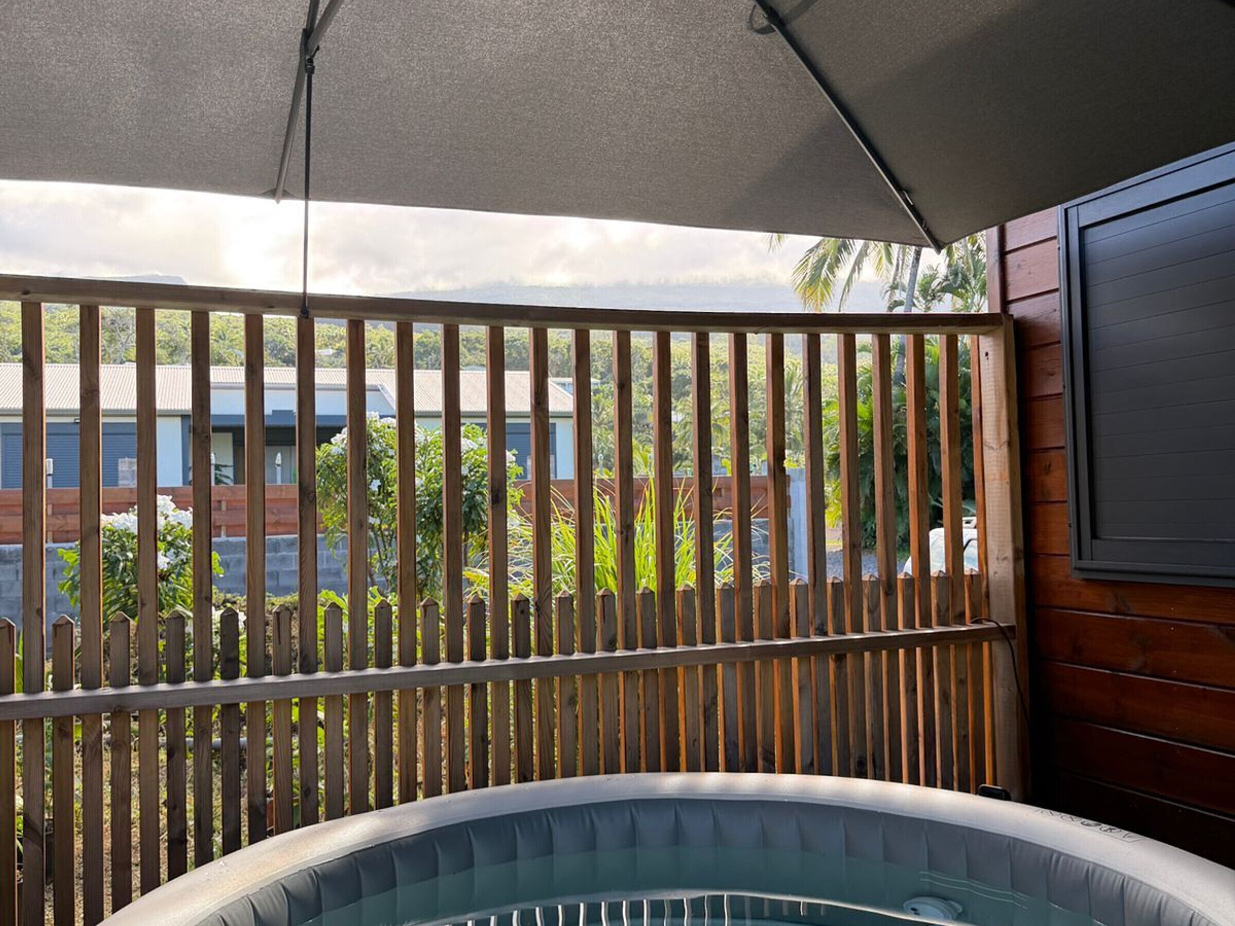 Ofurô sob área sombreada, com cerca de madeira e vista para área residencial.