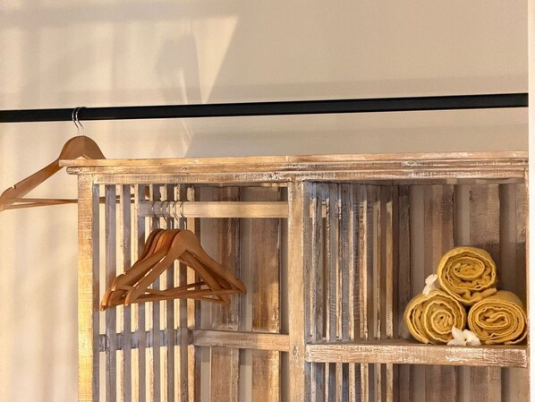 A rustic wooden shelf with a wooden hanger and rolled towels.