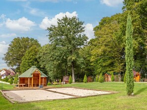 Eine rustikale Holzhütte mit grüner Dachdeckung, umgeben von einem gepflegten Rasen und hohen Bäumen.