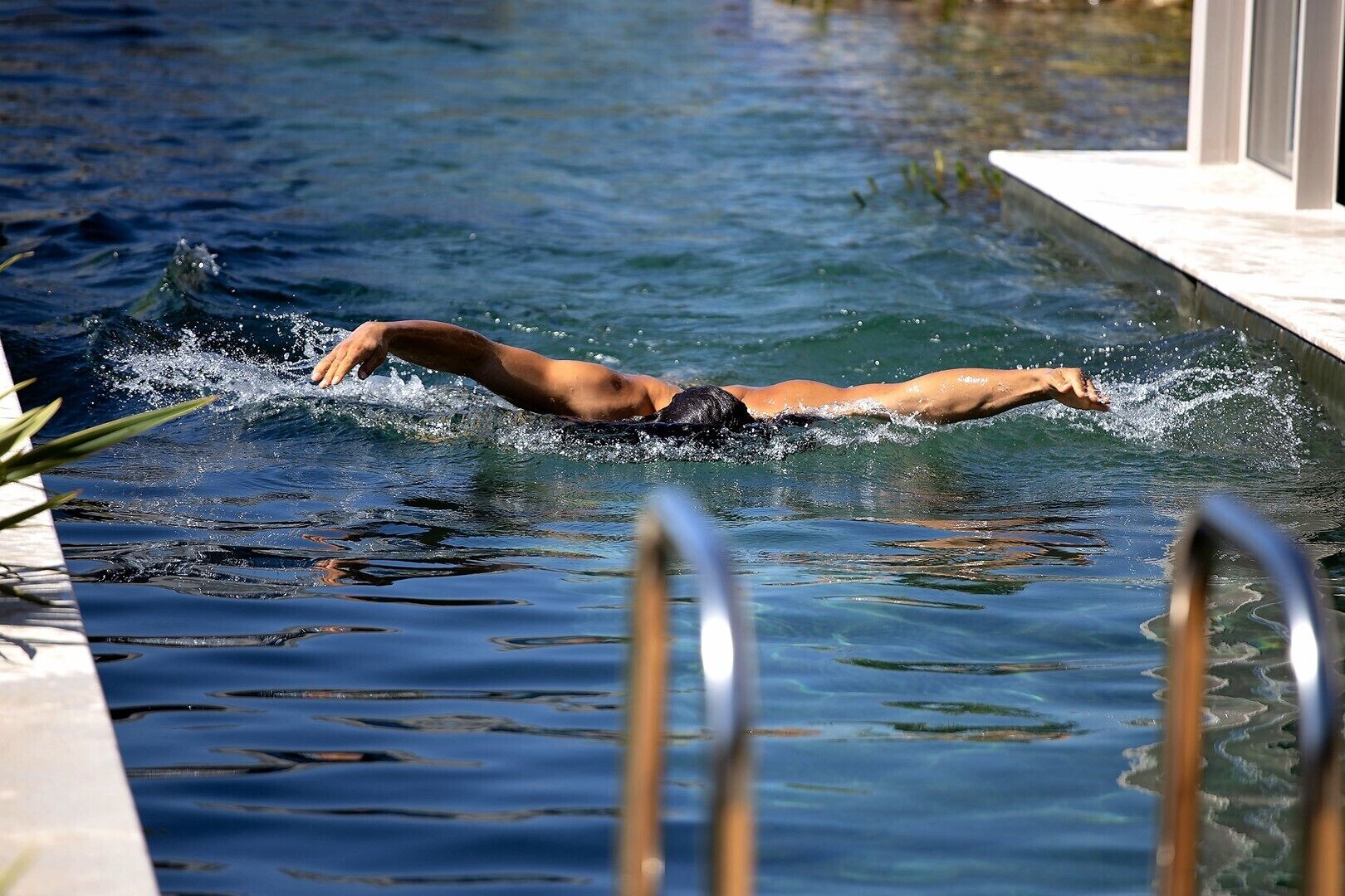 A swimmer in a pool with clear water, a poolside railing, and a tiled edge.