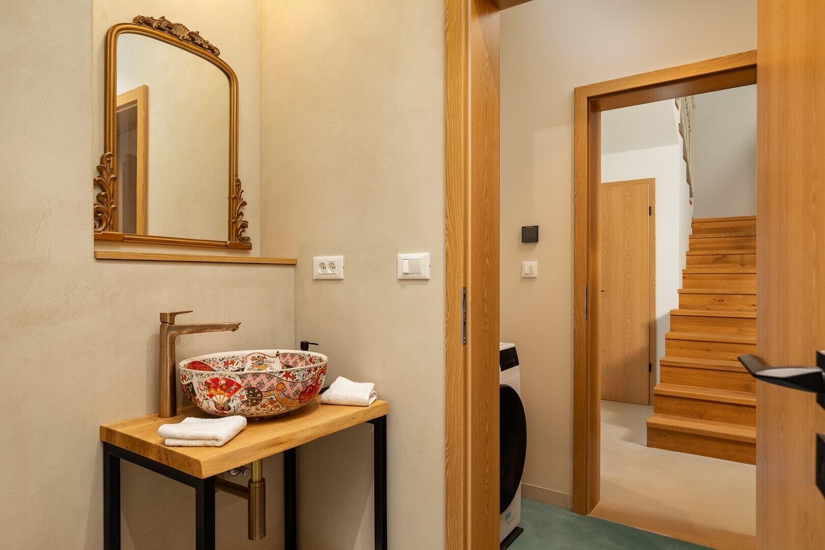 A bathroom with a wooden vanity, a large bowl sink, a mirror, and a staircase leading to another room.
