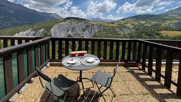Eine Terrasse mit gedecktem Tisch für zwei Personen mit Blick auf eine gebirgige Landschaft.