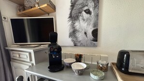 Eine Küchenzeile mit Kaffeemaschine, Schüsseln, Toaster und einem an der Wand montierten Fernseher.
