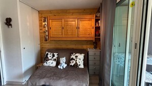 Ein Schlafzimmer mit einem Bett, Holzschränken, einem kleinen Schminktisch und einer Glastür.