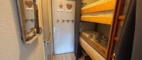 Un couloir étroit, avec un lit superposé sur la droite, une porte décorée de motifs en forme de cœur et un miroir sur la gauche.