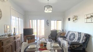 A dining area with a table set for four, a sofa, a television, and a window with curtains. - Beautiful 2-bed apt with sea view, glassed-in terrace, parking, 750m from the beach in Roses (Roses)