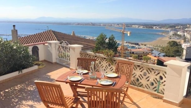 A terrace with a table set for two, overlooking a coastal cityscape with a bridge and mountains in the distance. - Beautiful 2-bed apt with sea view, glassed-in terrace, parking, 750m from the beach in Roses (Roses)