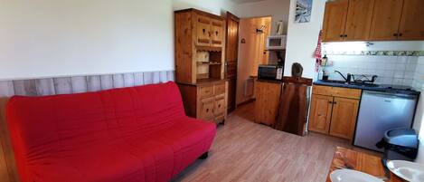 A compact living space with a red sofa, wooden cabinets, a kitchenette, and a dining area with a table set for two.