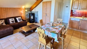 A cozy living room with a fireplace, a dining area with a table and chairs, and a kitchen with wooden cabinets. - Duplex with south-facing balcony - 5 guests (Saint-Michel-de-Chaillol)