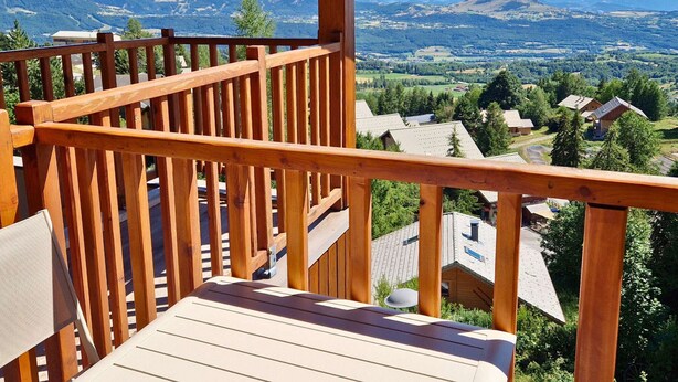 A wooden deck with a view of a mountainous landscape and residential buildings. - Duplex with south-facing balcony - 5 guests (Saint-Michel-de-Chaillol)