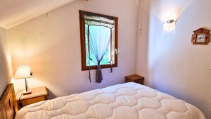 A bedroom with a bed, a window with curtains, a bedside lamp, a small wooden nightstand, and a wall-mounted clock. - Duplex with south-facing balcony - 5 guests (Saint-Michel-de-Chaillol)