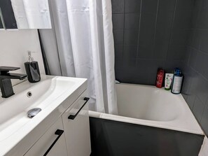 Et badeværelse med en hvid vask, haneføl i sort og et bruseområde med mørke fliser.
