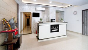 A modern reception area with a white reception desk, a mounted television, and a clock on the wall. - Collection O Tourist Complex Area (Agra)