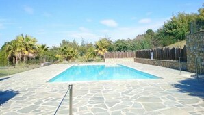 A rectangular swimming pool with a stone deck, surrounded by a wooden fence and palm trees. - Charming apartment, air conditioning - 2 guests (La Croix-Valmer)