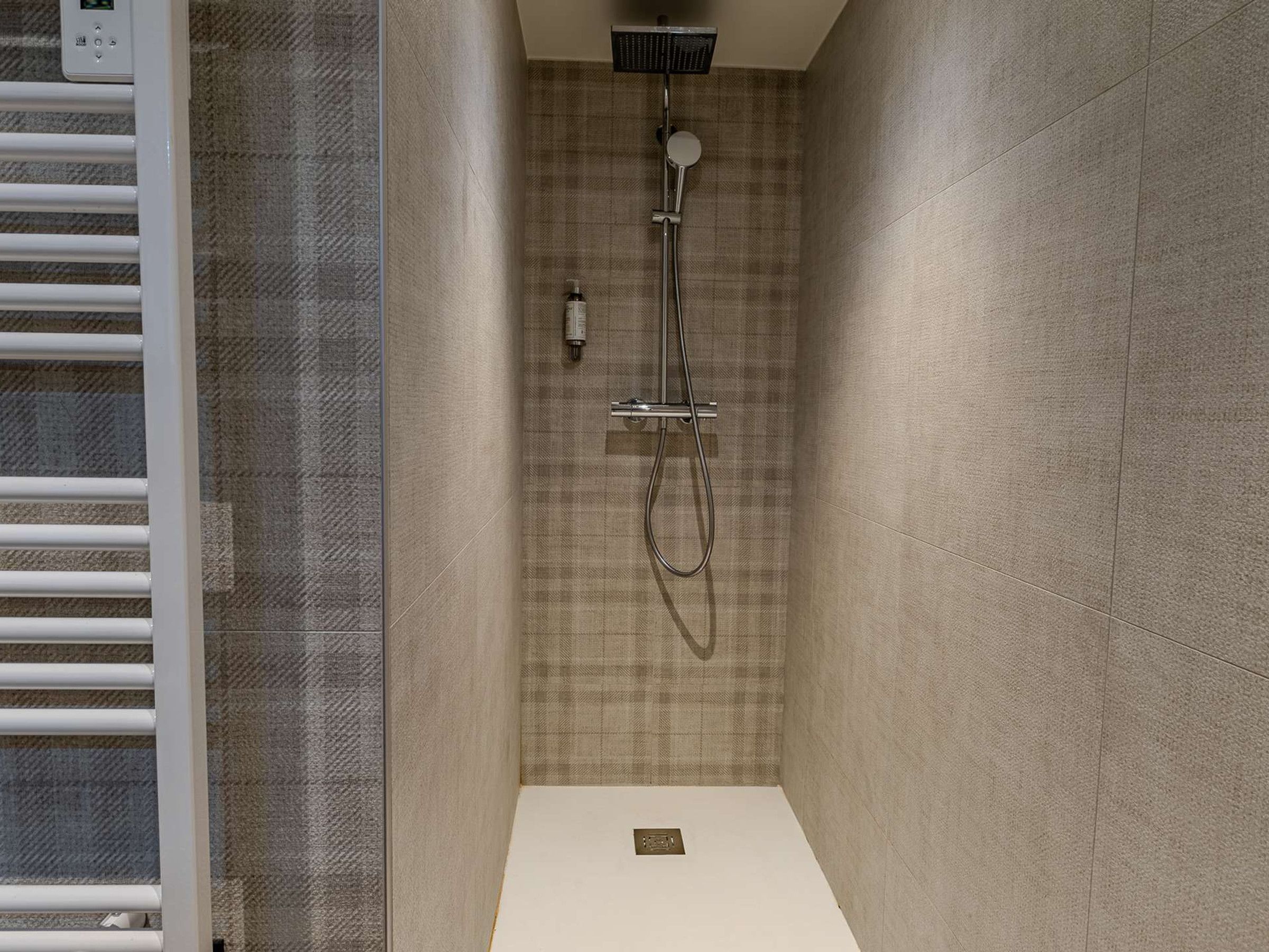 A shower with a handheld showerhead and a wall-mounted faucet.