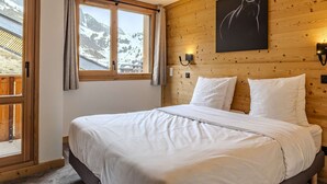 A bedroom with a wooden headboard, a bed with white bedding, a window with curtains, and a wall-mounted light fixture. - Luxury apartment, parking, 6 guests - Belle Plagne (Belle Plagne)