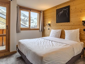 A bedroom with a wooden headboard, a bed with white bedding, a window with curtains, and a wall-mounted light fixture. - Luxury apartment, parking, 6 guests - Belle Plagne (Belle Plagne)