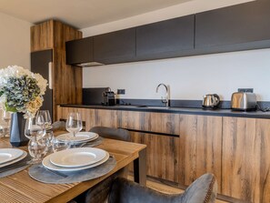 A modern kitchen with wooden cabinetry, a black countertop, and a dining area set with plates, glasses, and a vase of flowers. - Luxury apartment, parking, 6 guests - Belle Plagne (Belle Plagne)