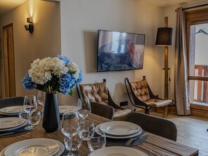 Ein Essbereich mit einem Tisch für vier Personen, einem Blumenstrauß und einem an der Wand befestigten Fernseher.