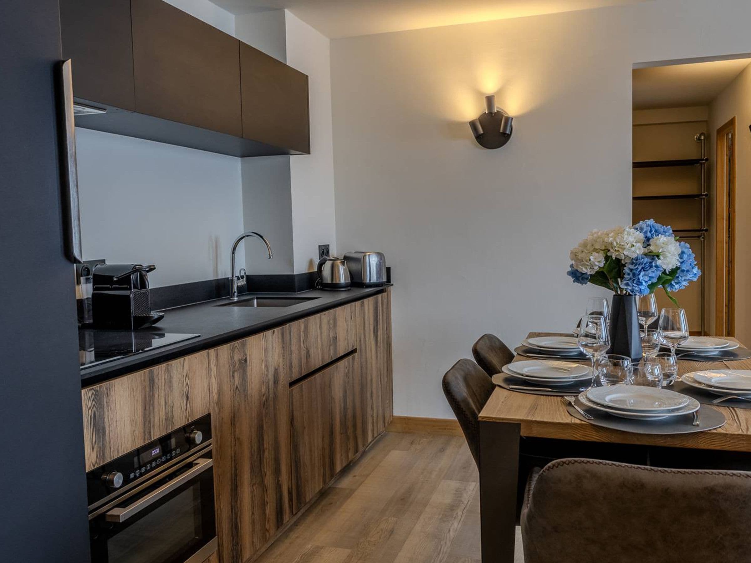 A modern kitchen with a built-in oven, a sink, and a dining area with a table set for four.