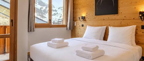 Ein Schlafzimmer mit einem großen Bett, Holzwänden, Blick auf die Berge und einem Katzenbild.