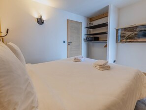 Ein Hotelzimmer mit einem Bett, einer Wandleuchte, einer Tür und einem Regal mit Handtüchern.