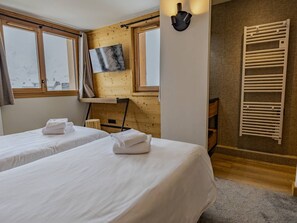 Et hotelværelse med to senge, et ophængt fjernsyn, en trævæg og en radiator.