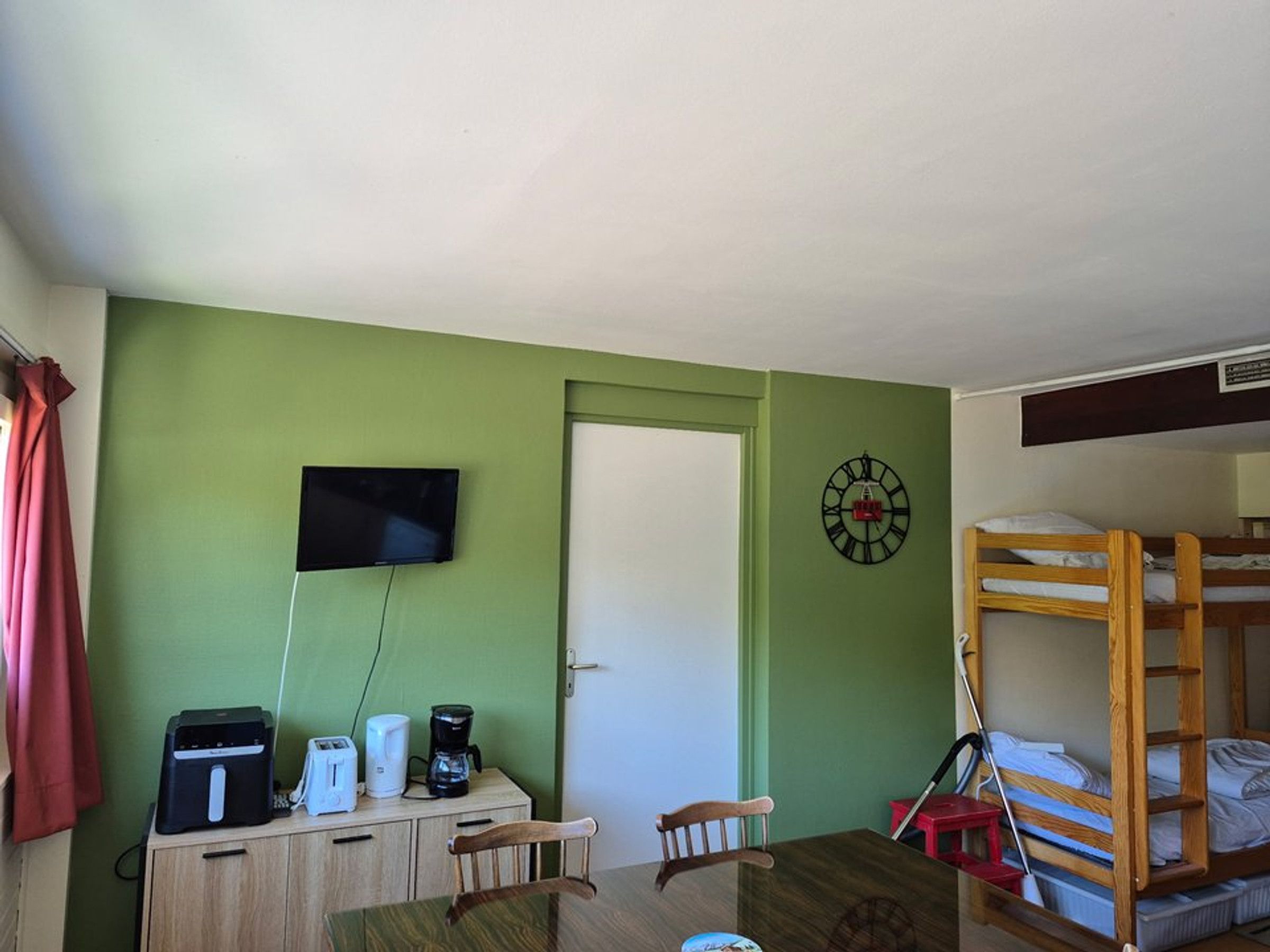 A room with a bunk bed, a desk with a television, a coffee maker, and a clock on the wall.