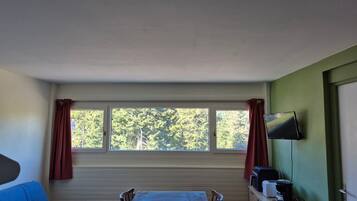 A room with a table and chairs, a television on the wall, and a window with curtains.