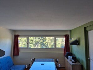 A room with a table and chairs, a television on the wall, and a window with curtains. - Cozy apartment in the heart of the resort (Le Lioran)