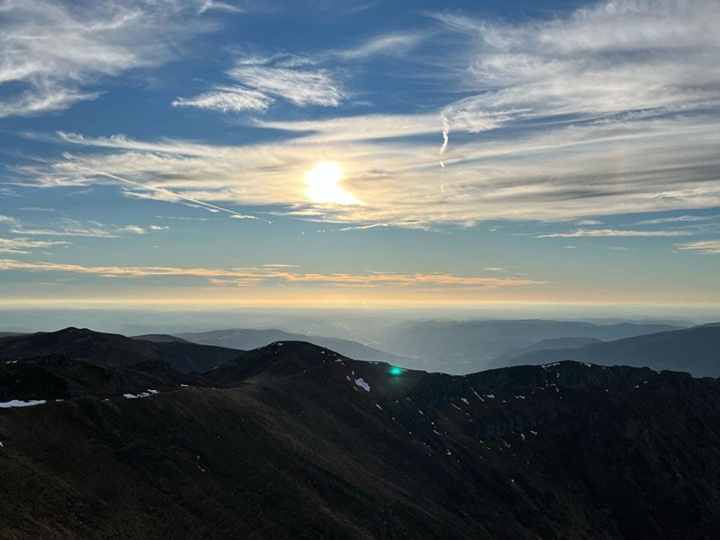 A mountainous landscape with a clear sky and the sun setting or rising.