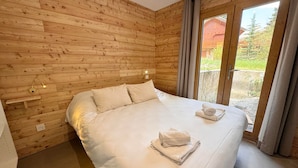 A wooden-paneled room with a bed, a small shelf, and a window with curtains. - Spacious chalet - 10 guests (Vars)