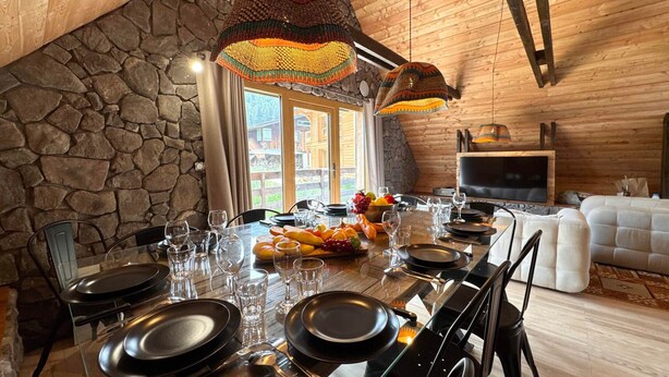 A dining area with a stone wall, wooden ceiling, and a large table set for six with plates, glasses, and a fruit bowl. - Spacious chalet - 10 guests (Vars)