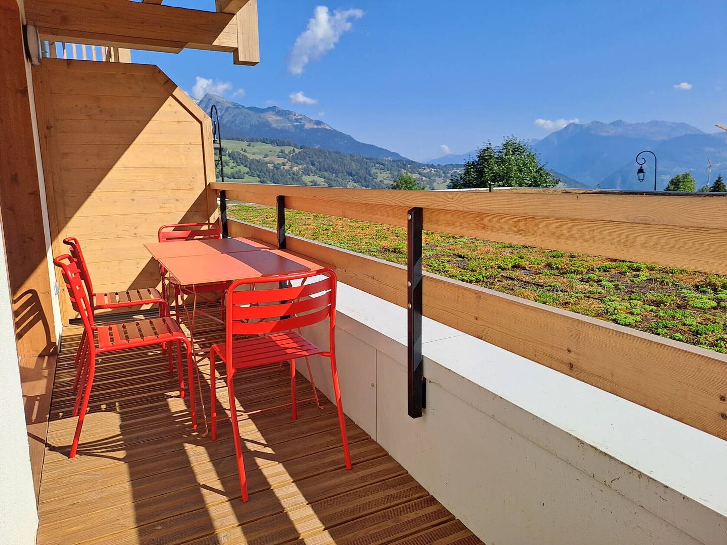 Une terrasse en bois avec une table et des chaises, donnant sur une zone herbeuse et des montagnes.