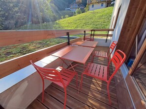 A balcony with a wooden railing, a table, and four red chairs. - Cozy apartment, mountain view - 6 guests (Valmorel)