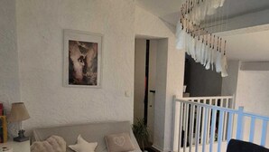 A living room with a sofa, a chair, a small table, a white wall with a framed picture, and a staircase with a railing. - *Ma bulle* private house (La Cadière-d'Azur)
