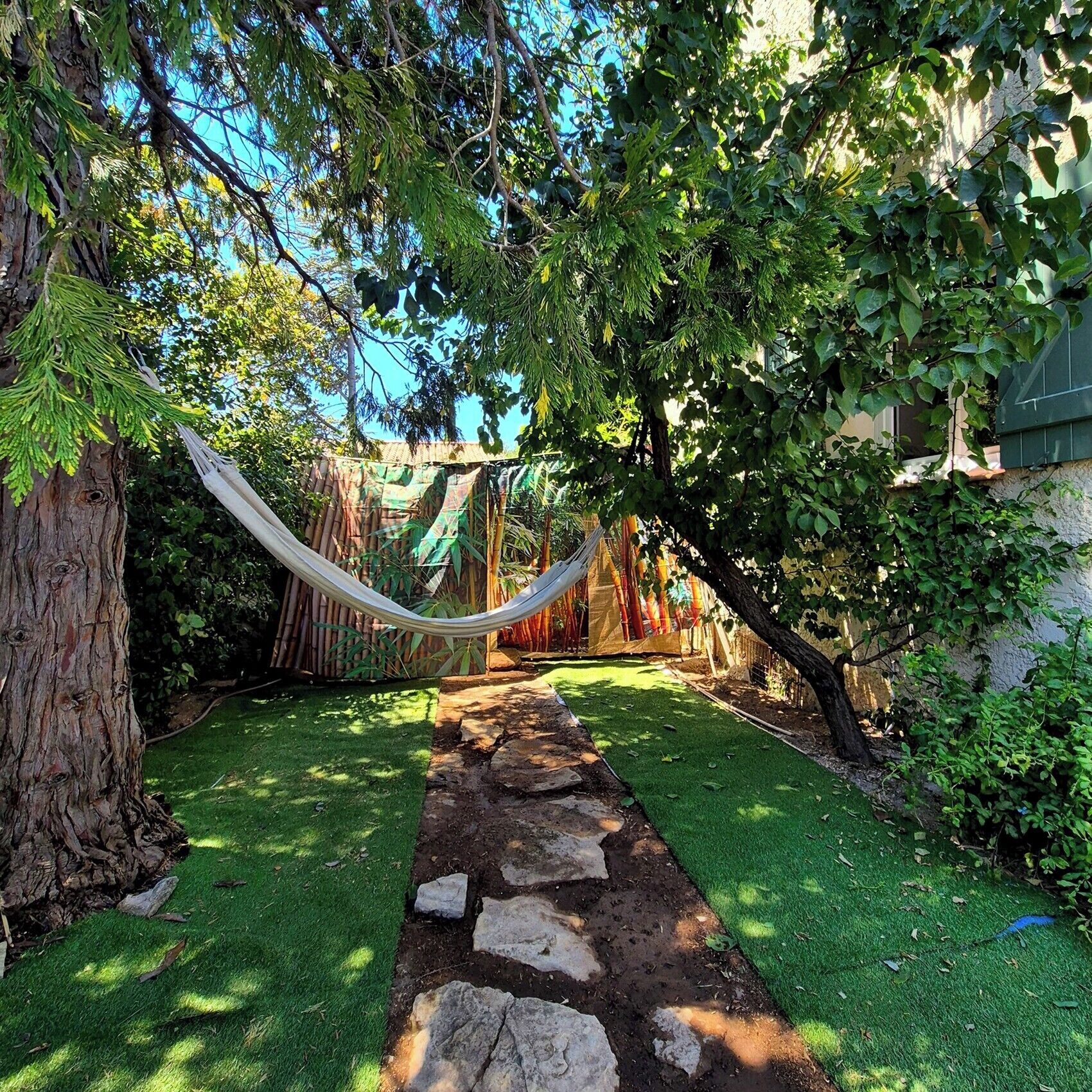 A garden path with a hammock, green grass, and trees.
