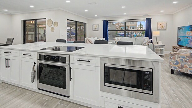 A modern kitchen with built-in appliances, a dining area with chairs, and a view of a pool and buildings. - Canal Front Retreat | Private Pool, Dock, and Game Room (Port Richey)