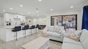 A modern kitchen with white cabinets, a dining area with a white table and chairs, and a living room with a white sofa and a coffee table. - Canal Front Retreat | Private Pool, Dock, and Game Room (Port Richey)