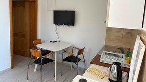 Una habitación pequeña y limpia con una mesa blanca, dos sillas, un televisor, una tetera y un armario.