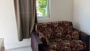 Una habitación con sofá, ventana con cortinas, aire acondicionado y suelo de baldosas.