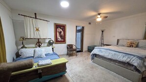 A bedroom with a bed, a sofa, a chair, a lamp, and a wall hanging. - Ahoy kids! Pirate's Grotto Apartment by Airport and Stadium (Tampa)