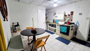 A compact kitchen with a dining table, chairs, a stove, microwave, and cabinets. - Ahoy kids! Pirate's Grotto Apartment by Airport and Stadium (Tampa)