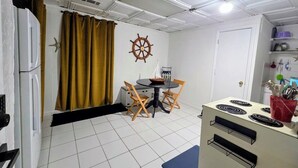 A compact kitchen with a stove, a dining table with chairs, a ship's wheel decoration, and a window with curtains. - Ahoy kids! Pirate's Grotto Apartment by Airport and Stadium (Tampa)