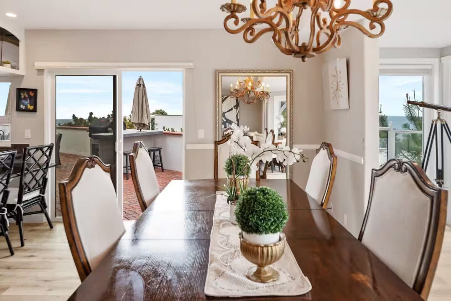 A dining room with a long table, chairs, and a chandelier. There are potted plants on the table.