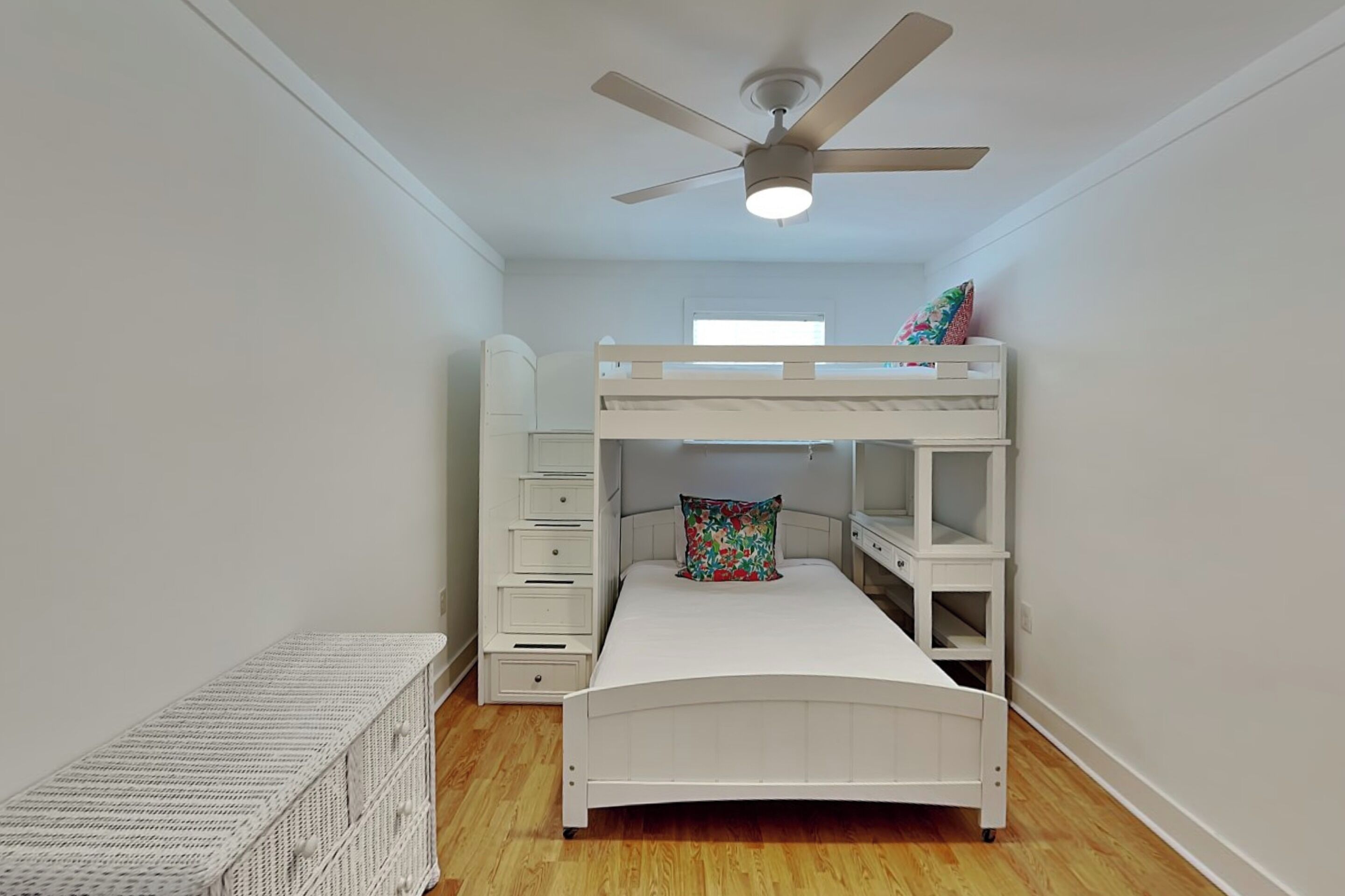 A bunk bed room with a ceiling fan, a window, and a white dresser.