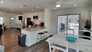 A modern kitchen with a central island, bar stools, a dining table with chairs, and a ceiling fan. - 50 Steps to the Beach | Spacious, Gas Grill, Beach Access (Tybee Island)