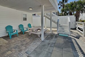 Une terrasse couverte avec des fauteuils Adirondack de couleur turquoise, une table de pique-nique et une clôture blanche.